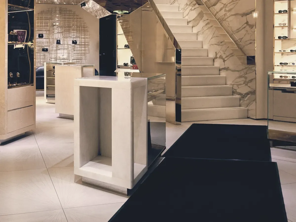 A luxury retail interior with stone floors, display plinths and a sculpted staircase
