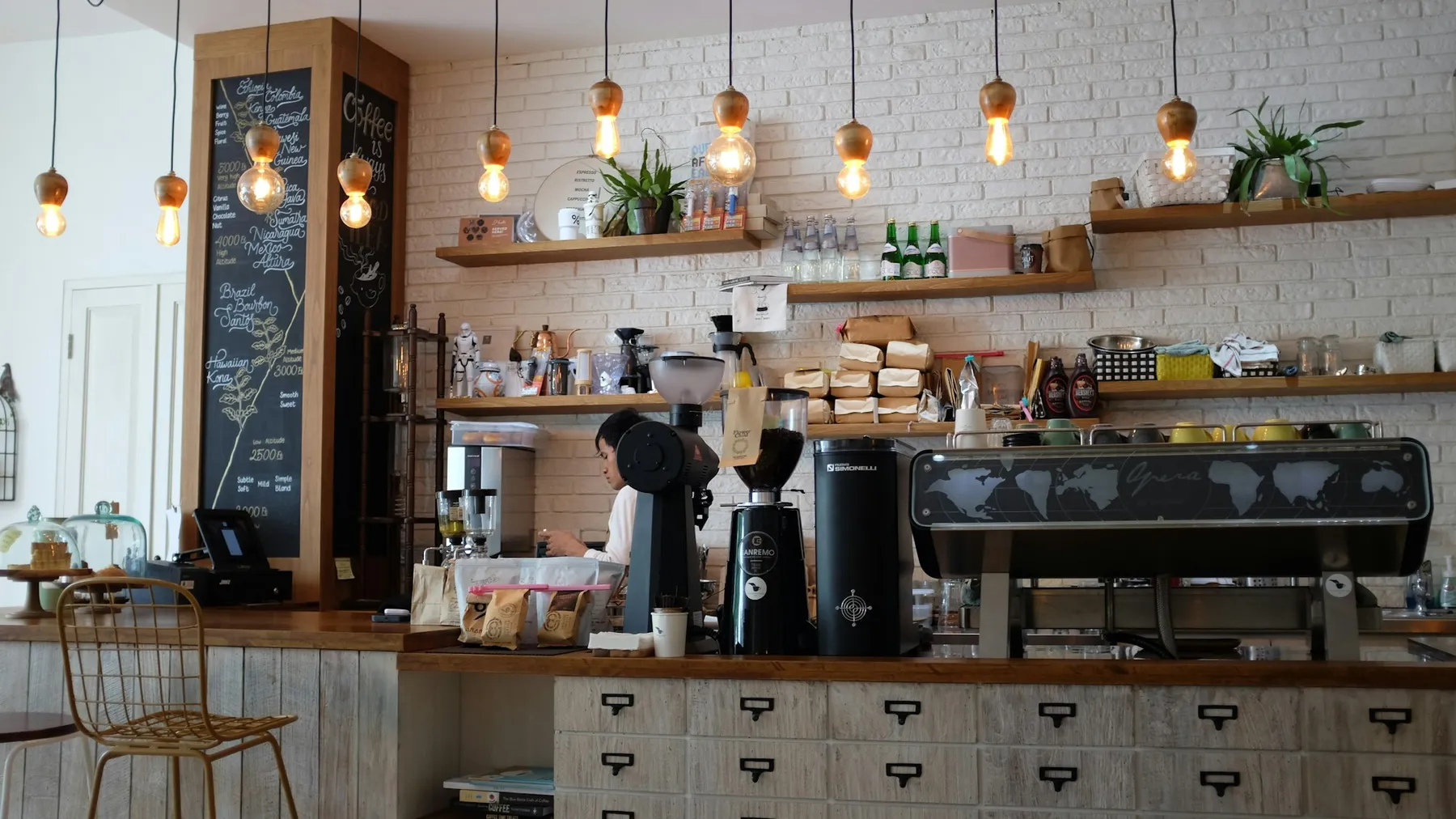 A café counter with an espresso machine, open shelving and warm pendant lights