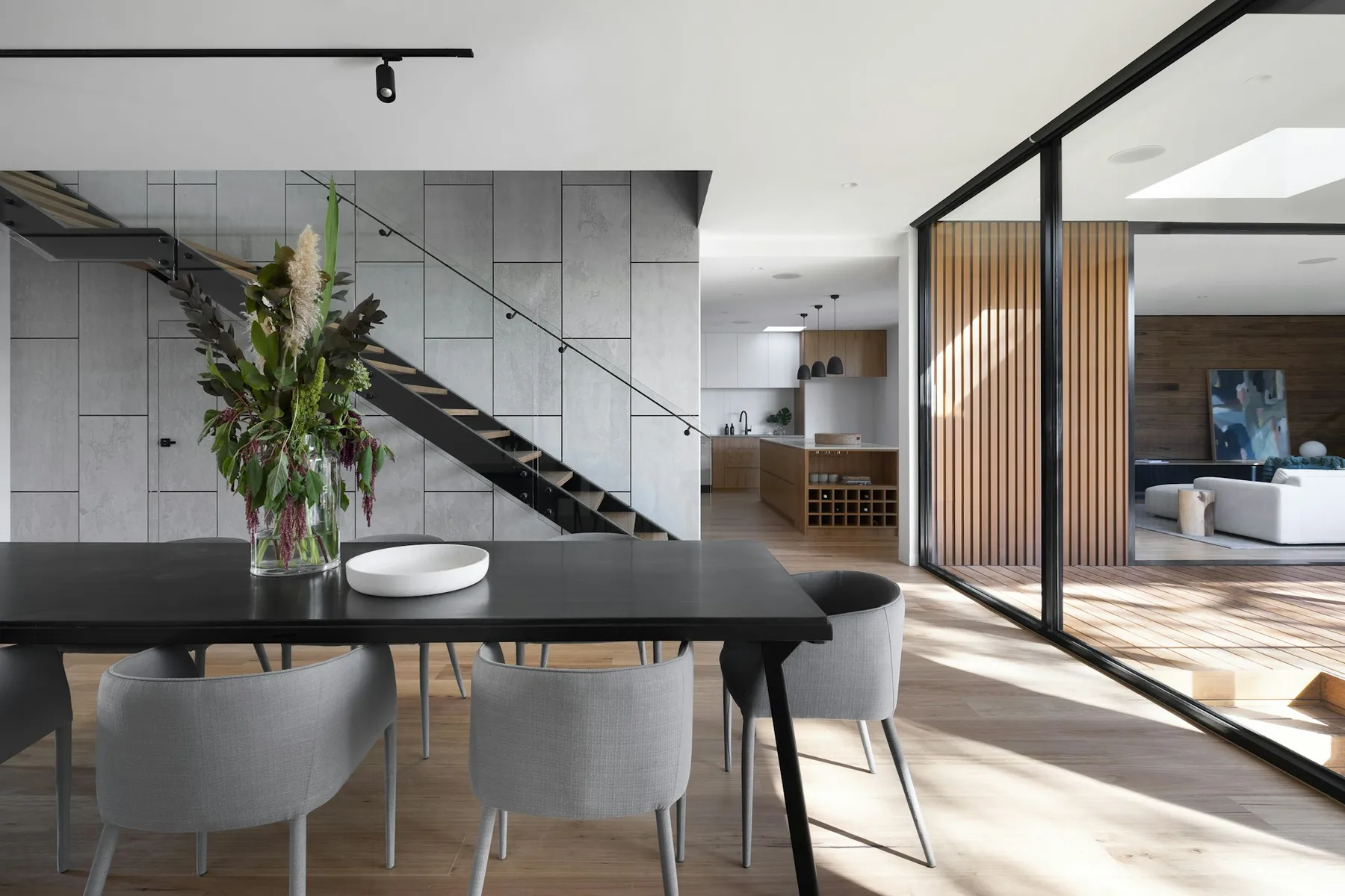 An open-plan dining and living space with a glass-railed staircase and pale grey walls