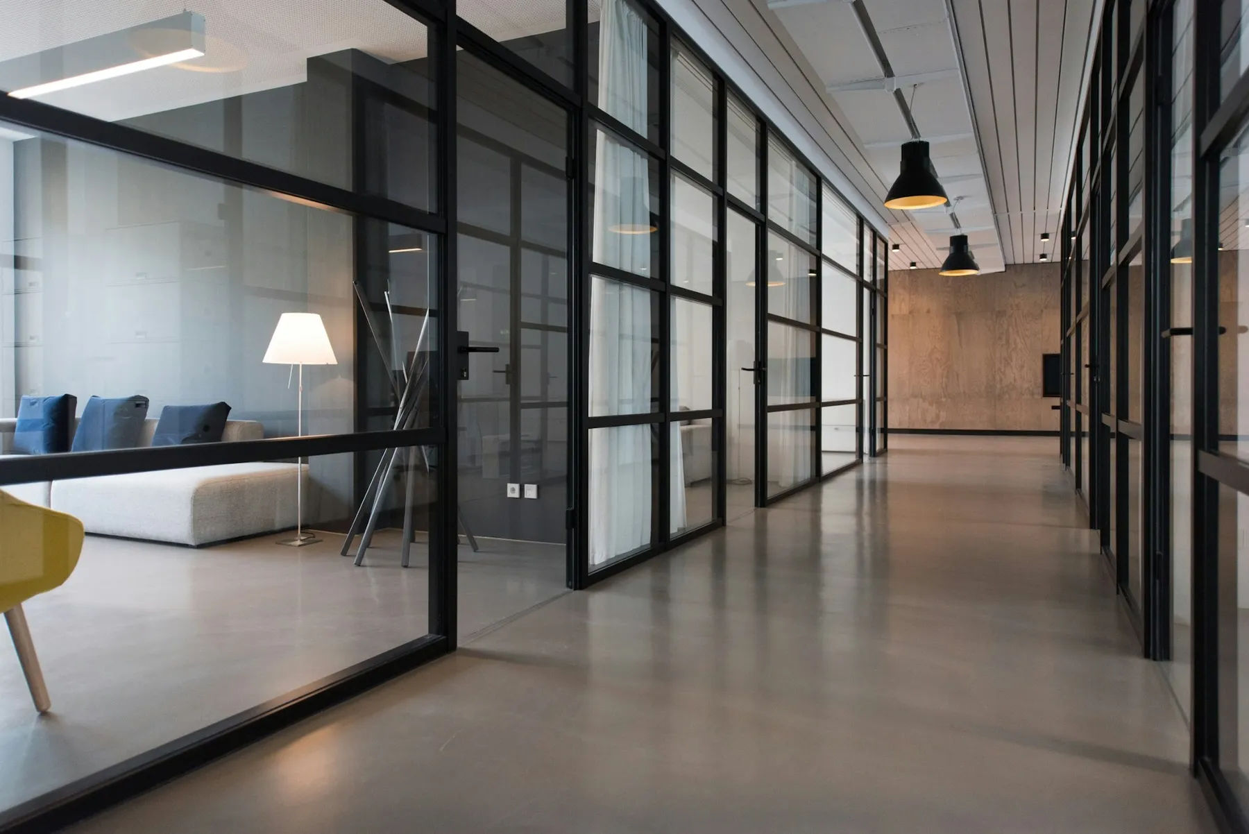 A modern office corridor with black-framed glass partitions and polished floors