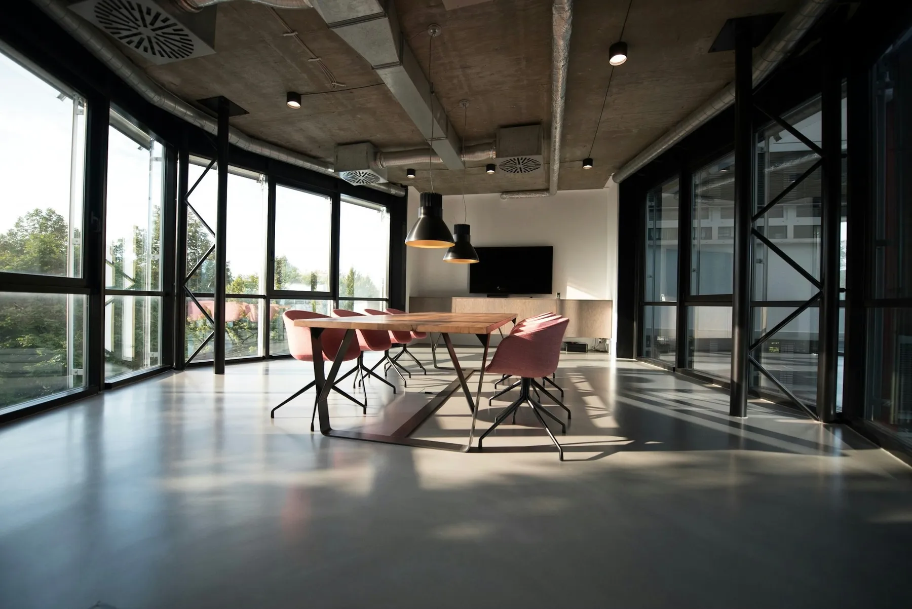 An open office with a raw ceiling, glass walls and a long work table